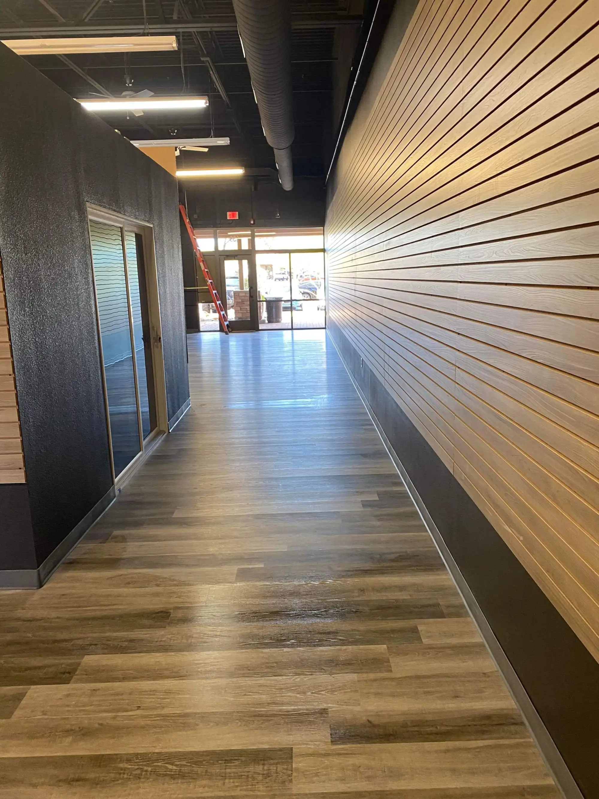 Freshly cleaned vinyl plank corridor in a commercial retail build-out, with wood slat wall and dark ceiling