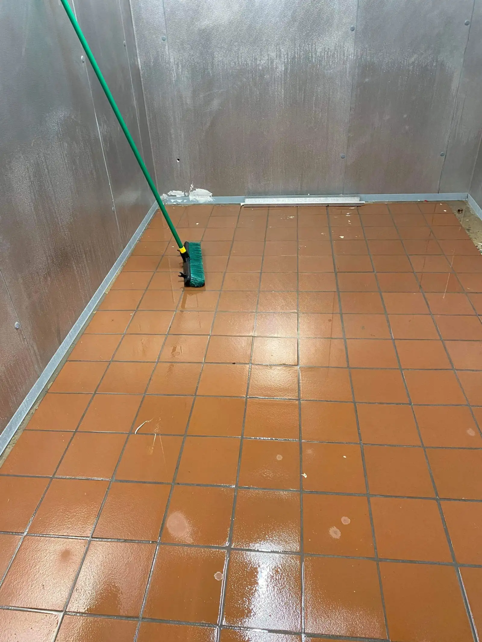 Wet terracotta tile floor mid-service with a floor squeegee during a deep clean